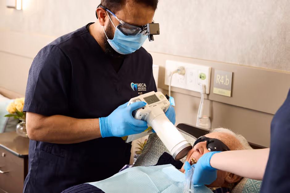 Smiling female nurse in blue scrubs talks with another person in a brightly lit medical setting.