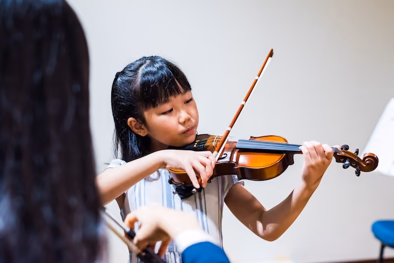 A young student concentrating as she plays the violin.