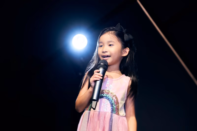 A young girl holding a microphone and happily singing.