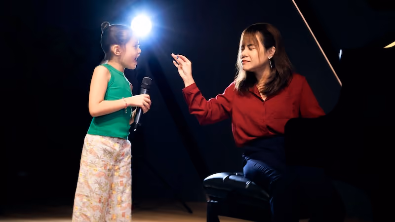 A young student (green) is singing her heart out as her teacher (red) conducts her pitch with her hands.