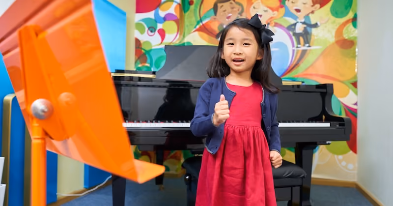 A young student attending music class. She is giving a thumbs up.
