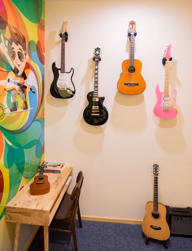 A music school studio with a number of guitars and ukuleles ranging from electric, to classical and even a hot pink edition!