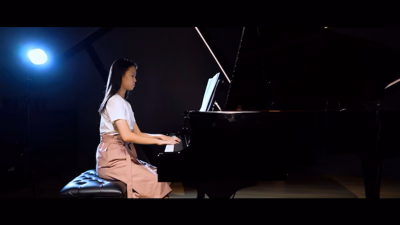 A teenage girl playing the grand piano in a recital hall.