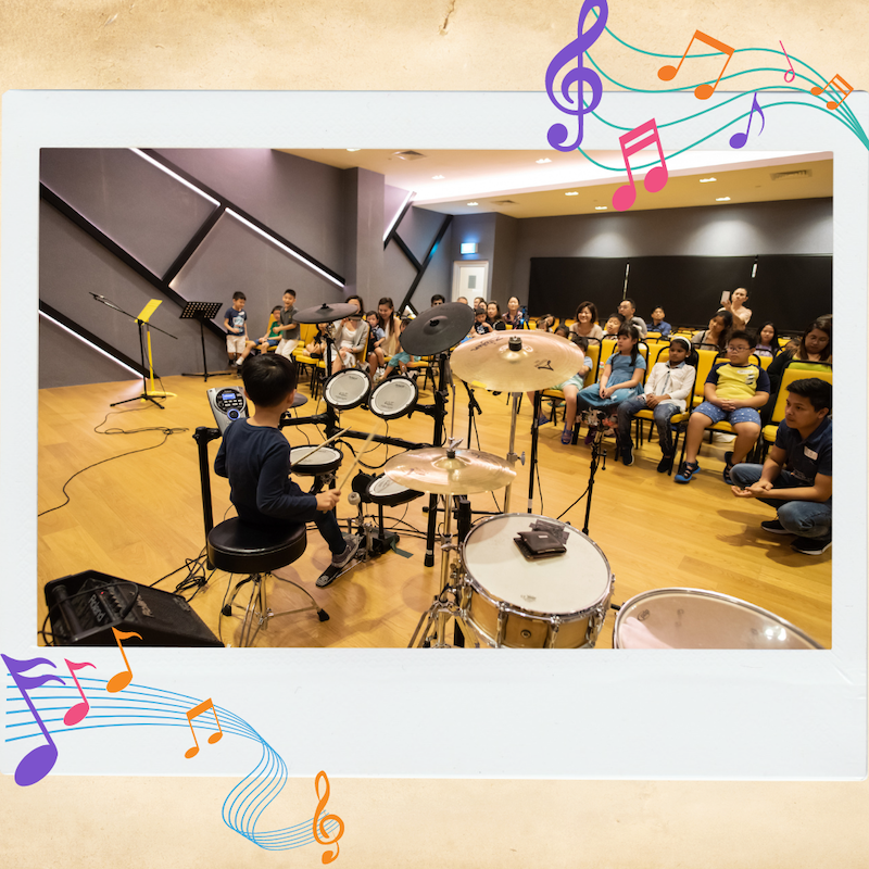 A child performing on the drums in front of his peers at a music studio.
