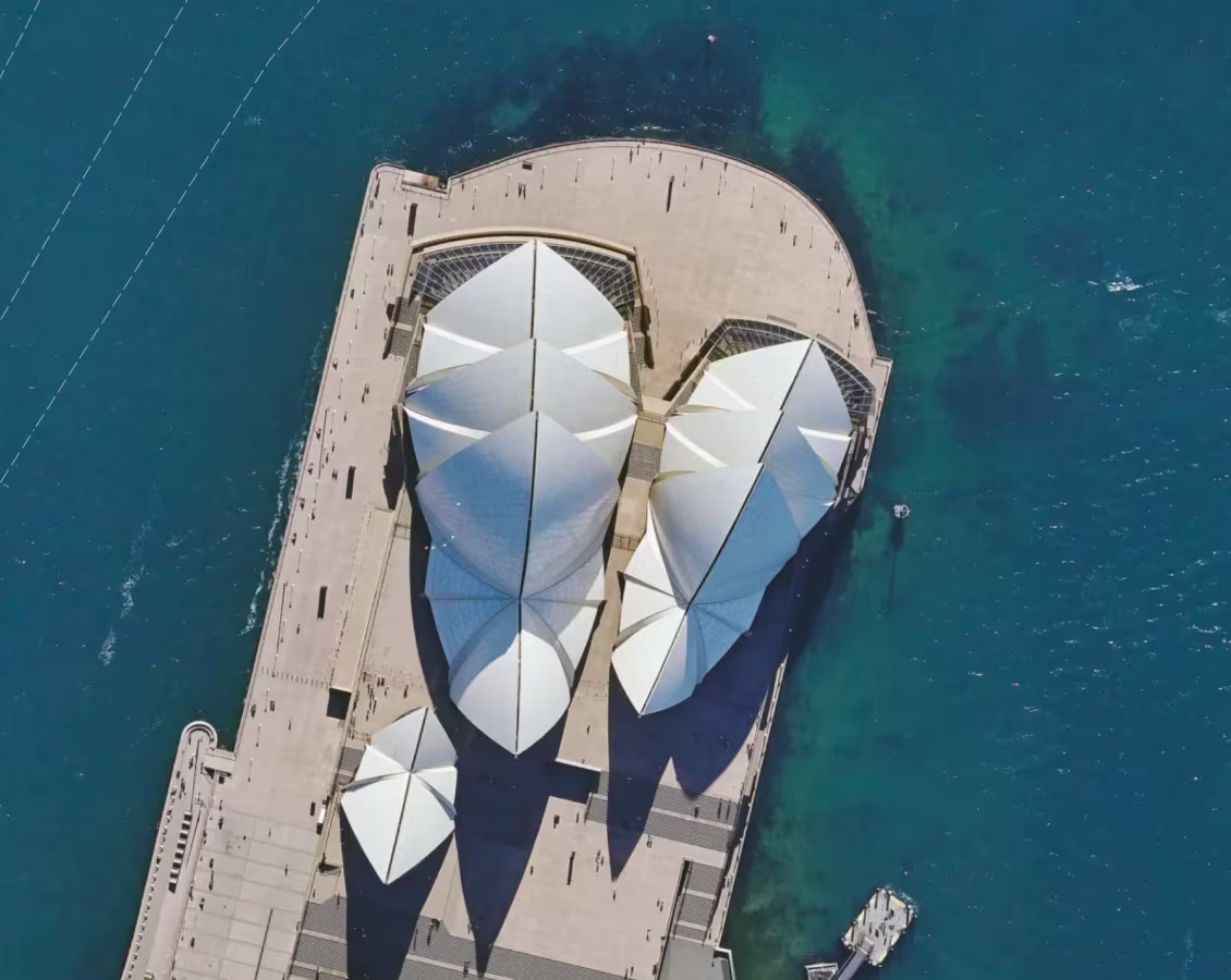 Aerial view of the Sydney Opera House with its white sail-like roof structures surrounded by blue water.