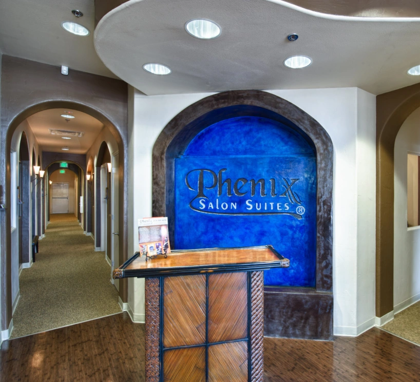 Interior hallway with a wooden podium and a blue sign reading Phenix Salon Suites on the wall.