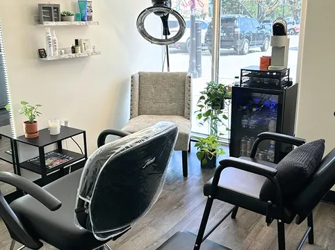 Modern salon suite with black chairs, small plants, product shelf, and large window showing street outside.