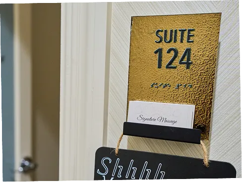 Gold textured door sign reading Suite 124 with a card holder containing a Signature Massage card.