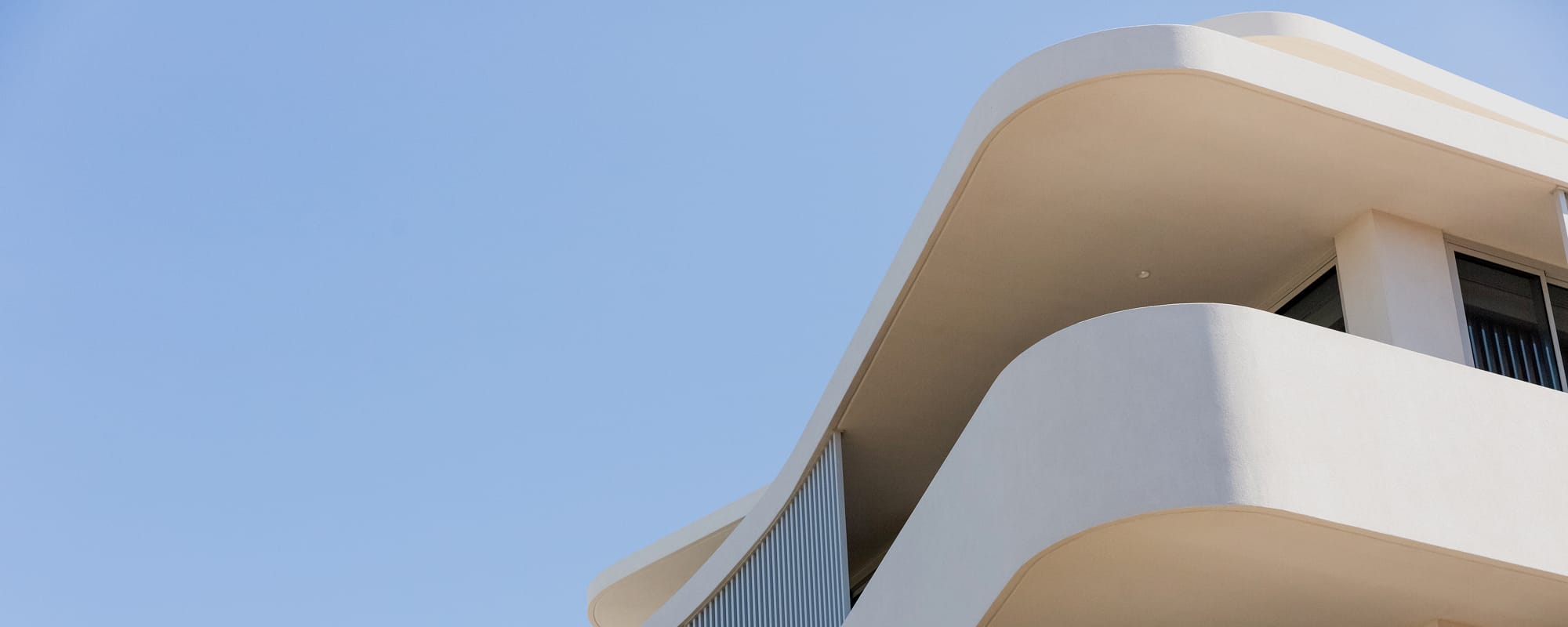 Modern curved white apartment balcony against a clear blue sky