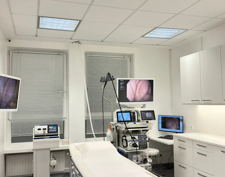 Drei Personen, zwei Ärzte und eine Frau in Business-Kleidung, die in einem modernen Krankenhausflur über ein digitales Tablet sprechen.
