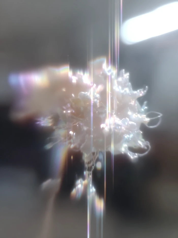 Glowing crystal cluster emitting vertical rainbow light beams with a blurred gray background.