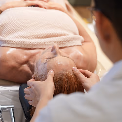 Une femme allongée recevant un massage du visage dans un spa ou institut de beauté.