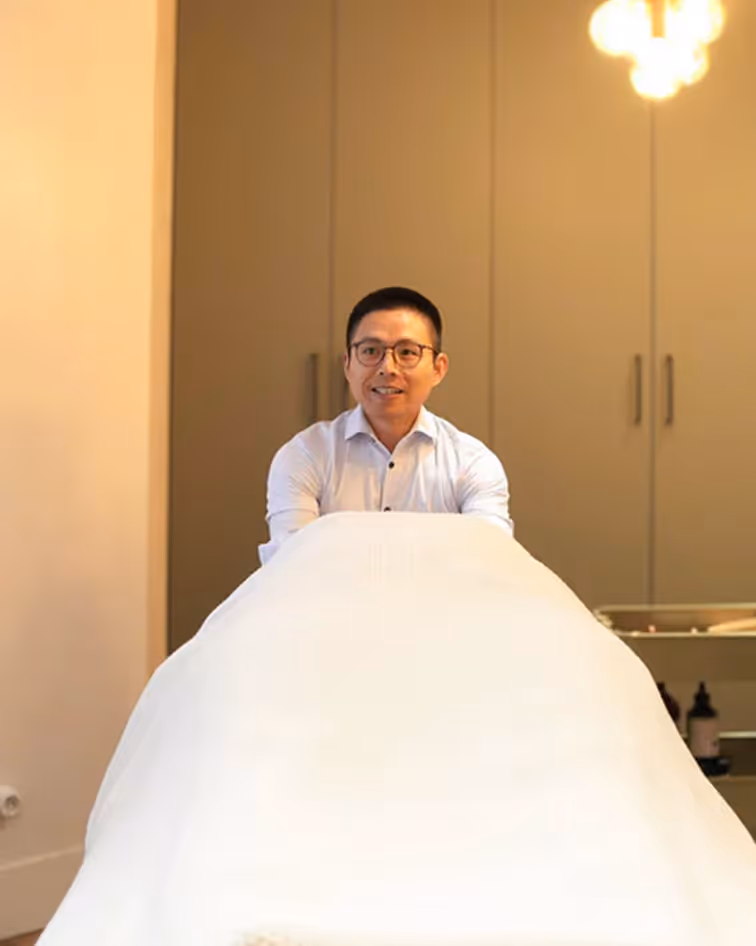 Un homme souriant portant une chemise blanche est assis derrière une table recouverte d'une nappe blanche.