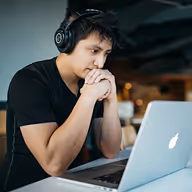 Jeune homme pensif avec casque assis devant un ordinateur portable Apple dans un café.