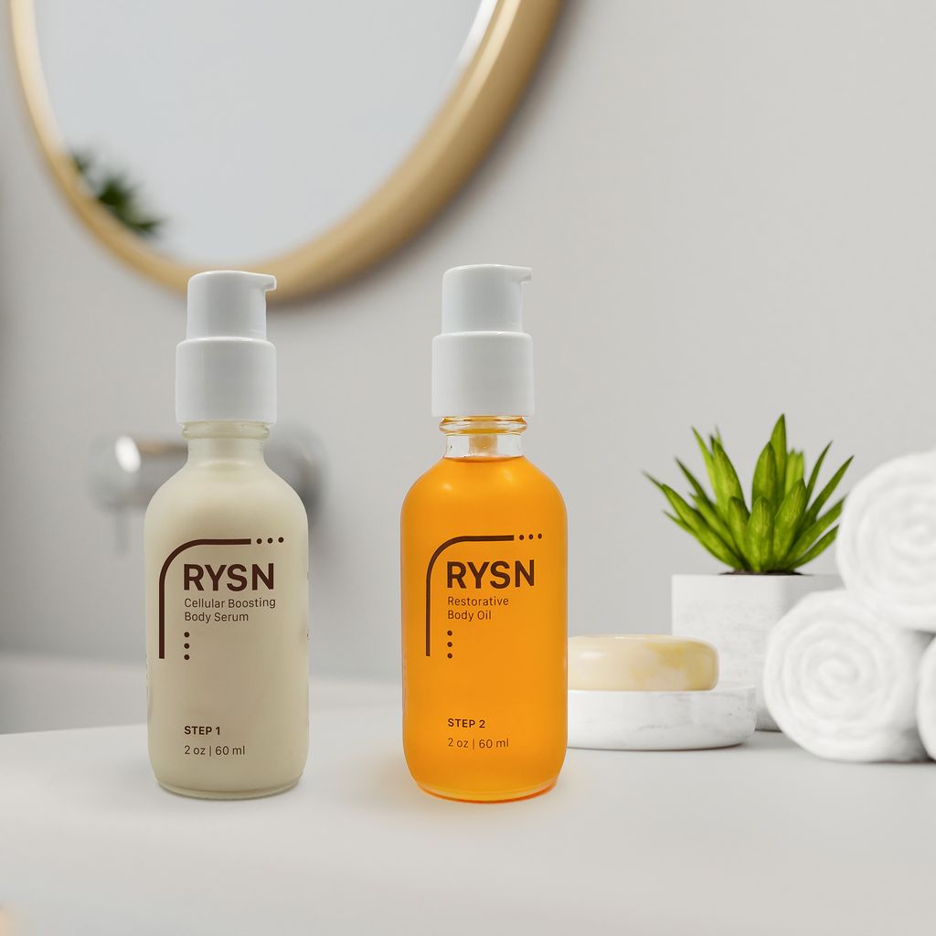Two white rectangular boxes of RYSN skincare products on a brown pine needle forest floor with a pine cone beside them; the left box is Cellular Boosting Body Serum labeled Step 1, and the right box is Restorative Body Oil labeled Step 2, each with brief benefits listed.