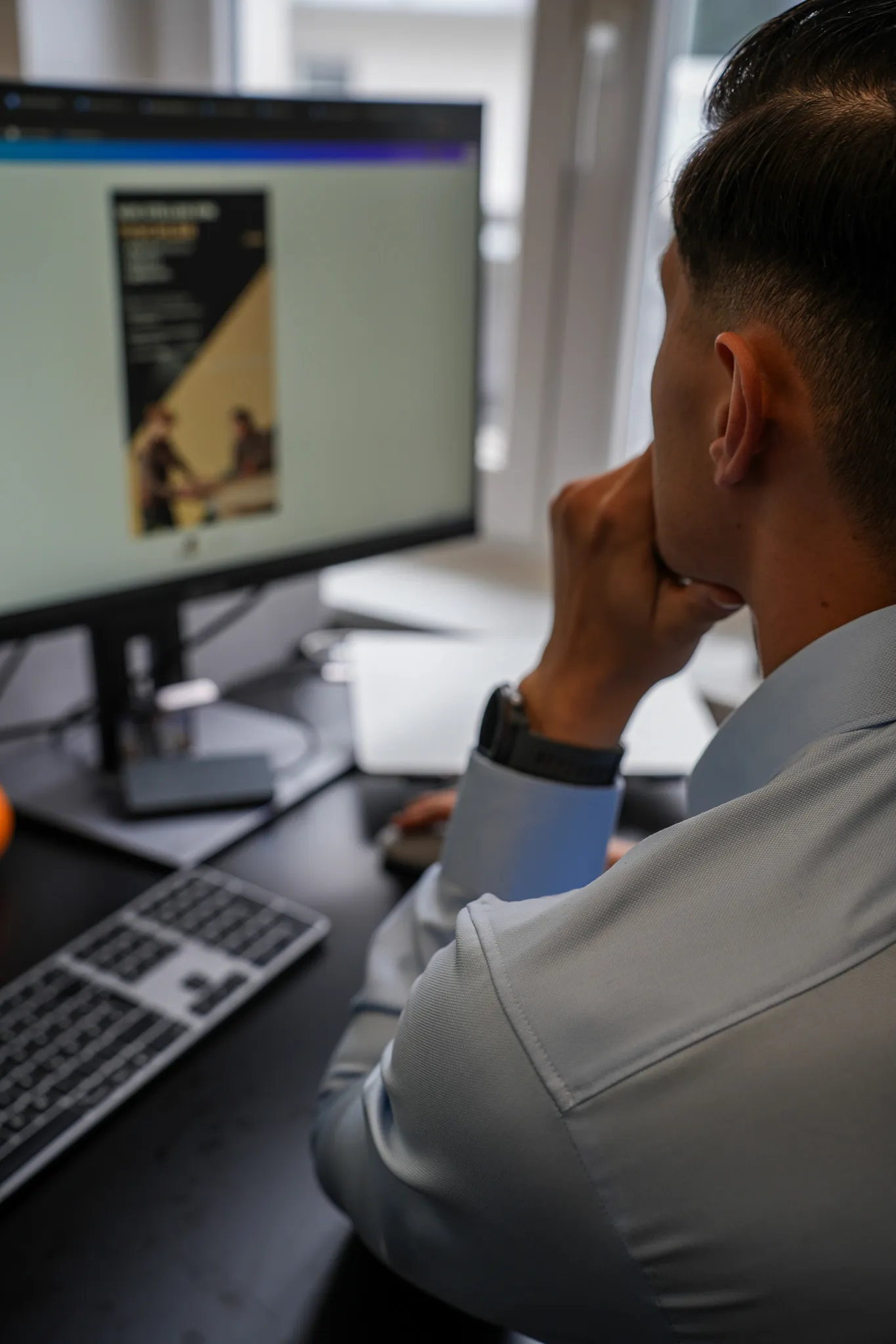 Man in blue shirt viewing a document on a computer monitor at a desk with keyboard and mouse.