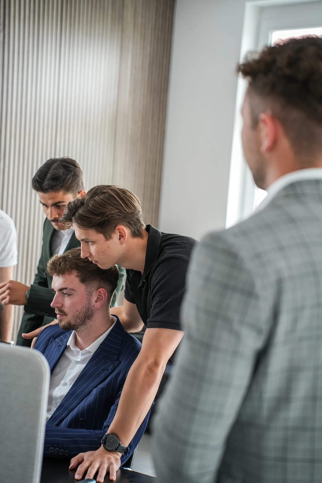 Young men gathered around a laptop, focused on the screen in a modern office setting.