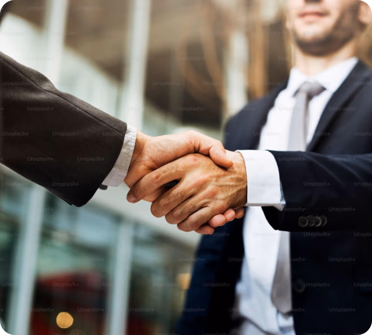 Two businessmen in suits shaking hands in an office building lobby.