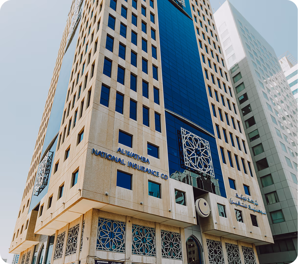 Perspective view looking up at a modern high-rise building with beige stone and blue glass facade, displaying the sign 'Al Wathba National Insurance Co'.
