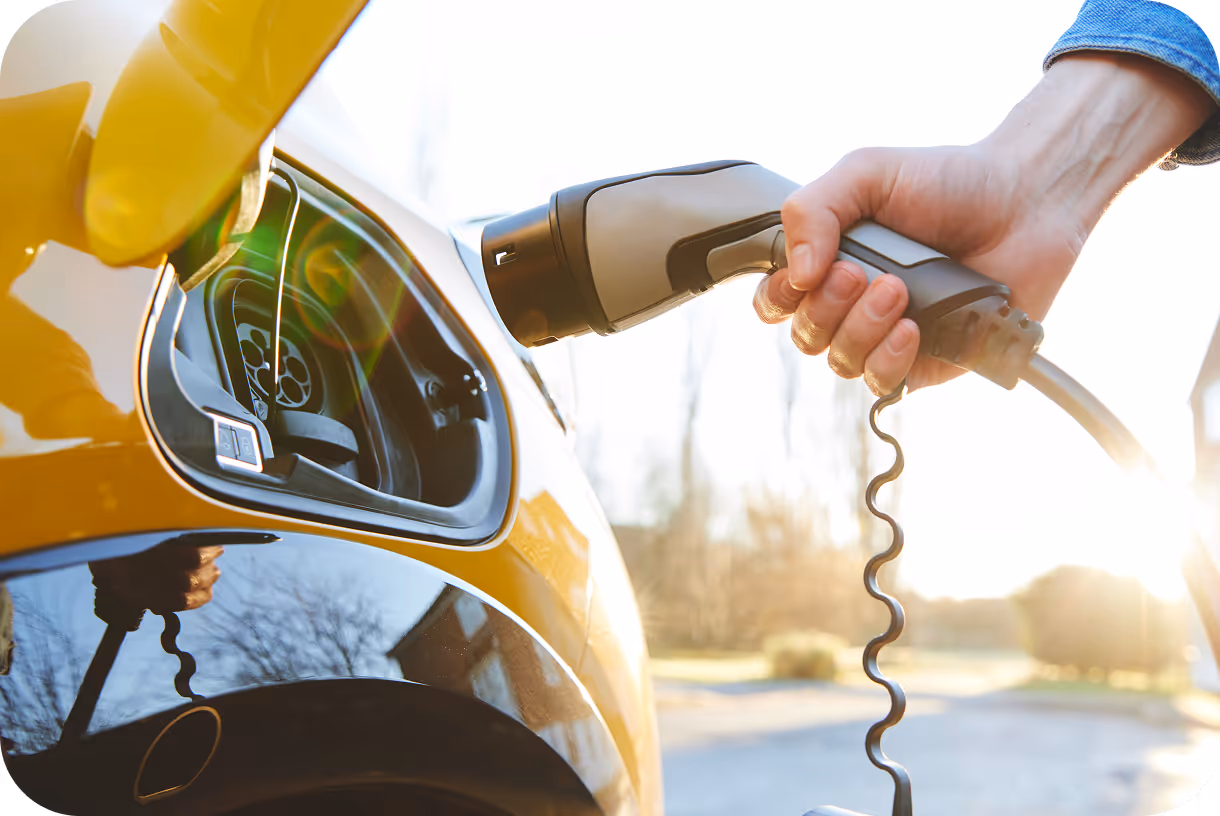 Hand plugging a charging cable into a yellow electric car during daylight.
