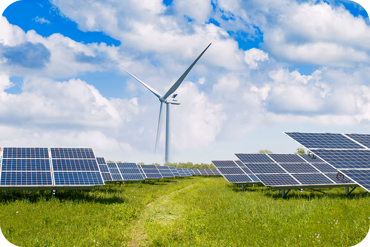 Solar panels installed on a green field with a wind turbine in the background under a partly cloudy blue sky.