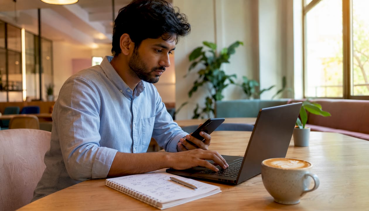 Man multitasking with phone and laptop at café