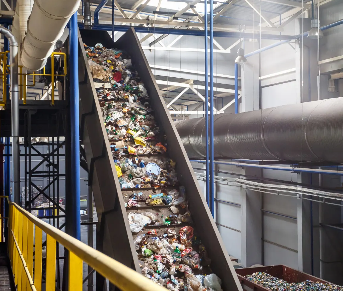 Müll und Plastikflaschen werden auf einem Förderband in einer Recyclinganlage transportiert.