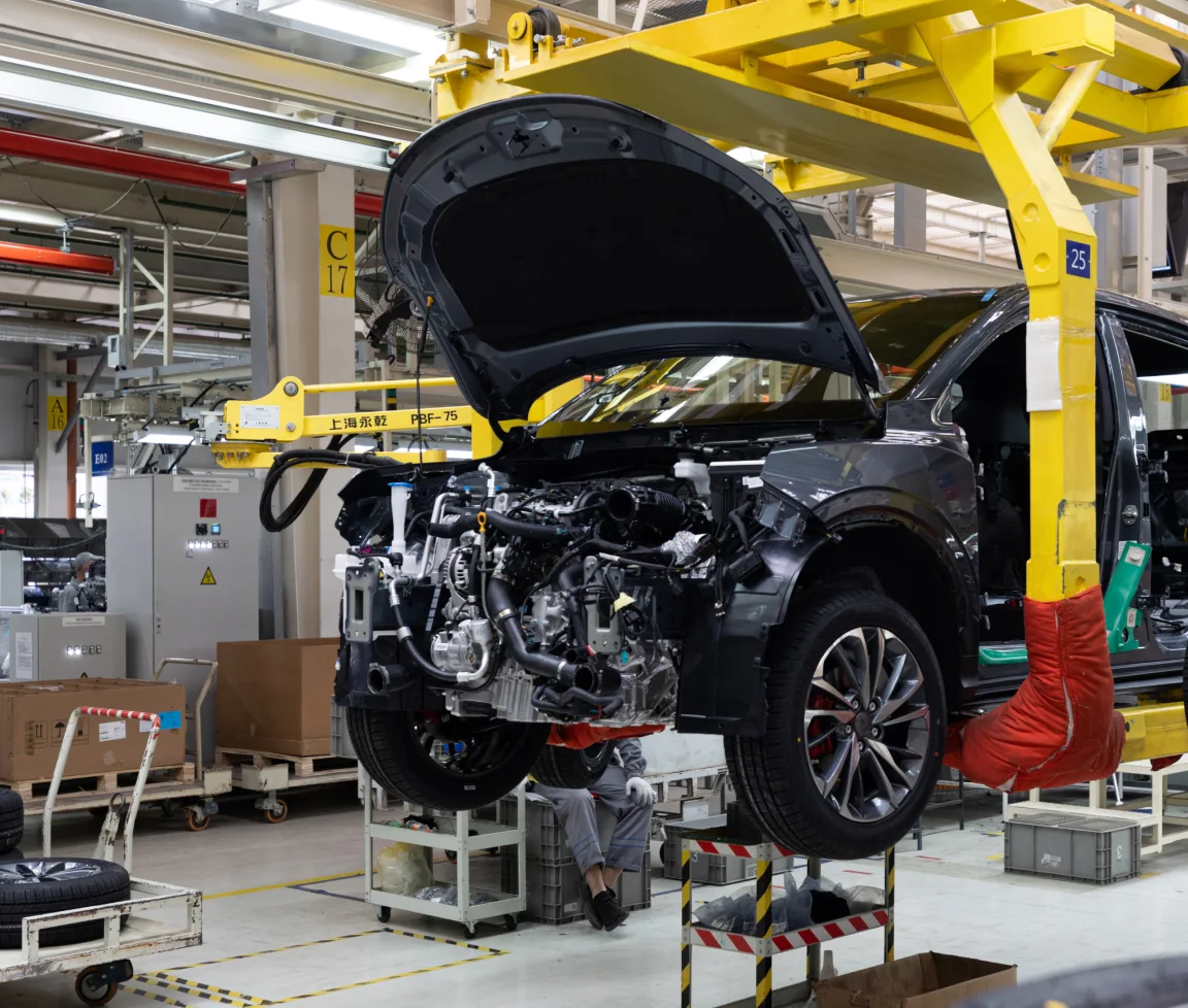 Schwarzes Auto mit geöffneter Motorhaube in moderner Autofabrik, angehoben an gelbem Hebearm.