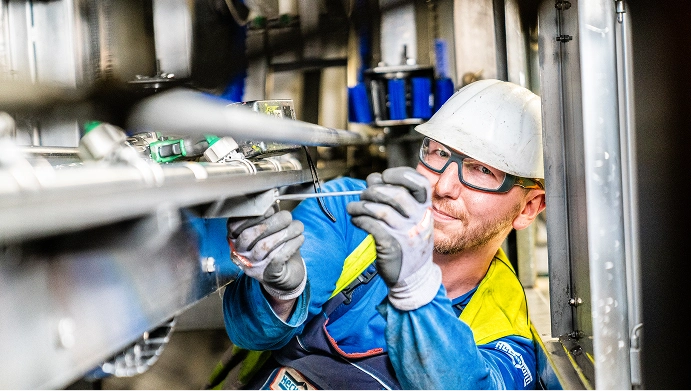 Ein Techniker mit Schutzhelm und Handschuhen arbeitet an Rohrleitungen in einer Industrieanlage.