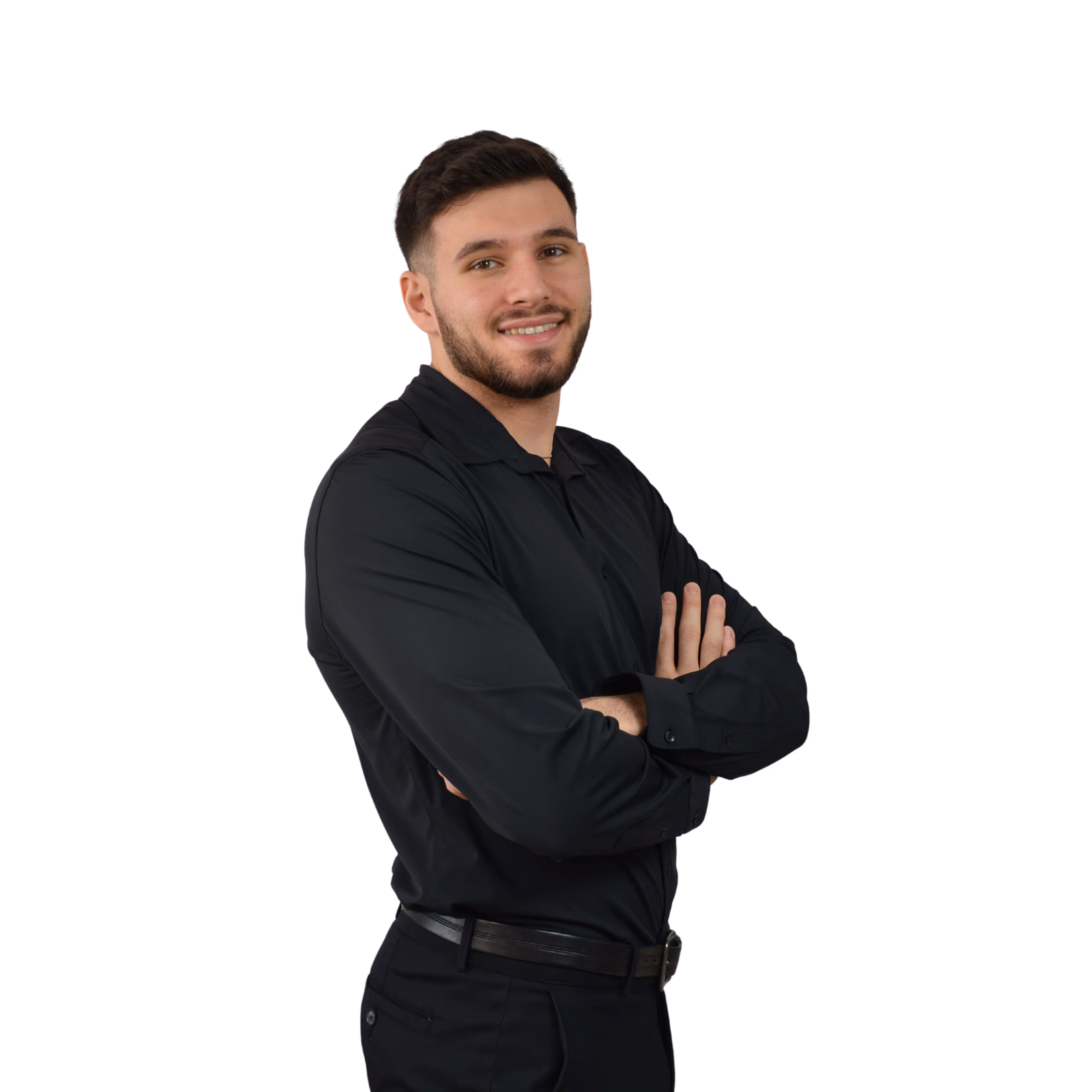 Smiling man with beard wearing black shirt and pants, arms crossed, standing against black background.