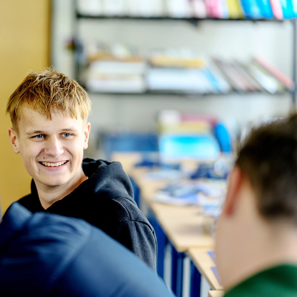Mladý student se usmívá a komunikuje s dalšími lidmi v učebně s regály knih.