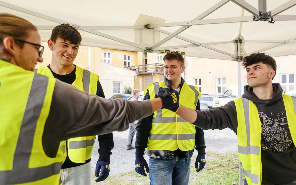 Čtyři studenti v reflexních vestách si při workshopu plácají pěstmi pod přístřeškem.