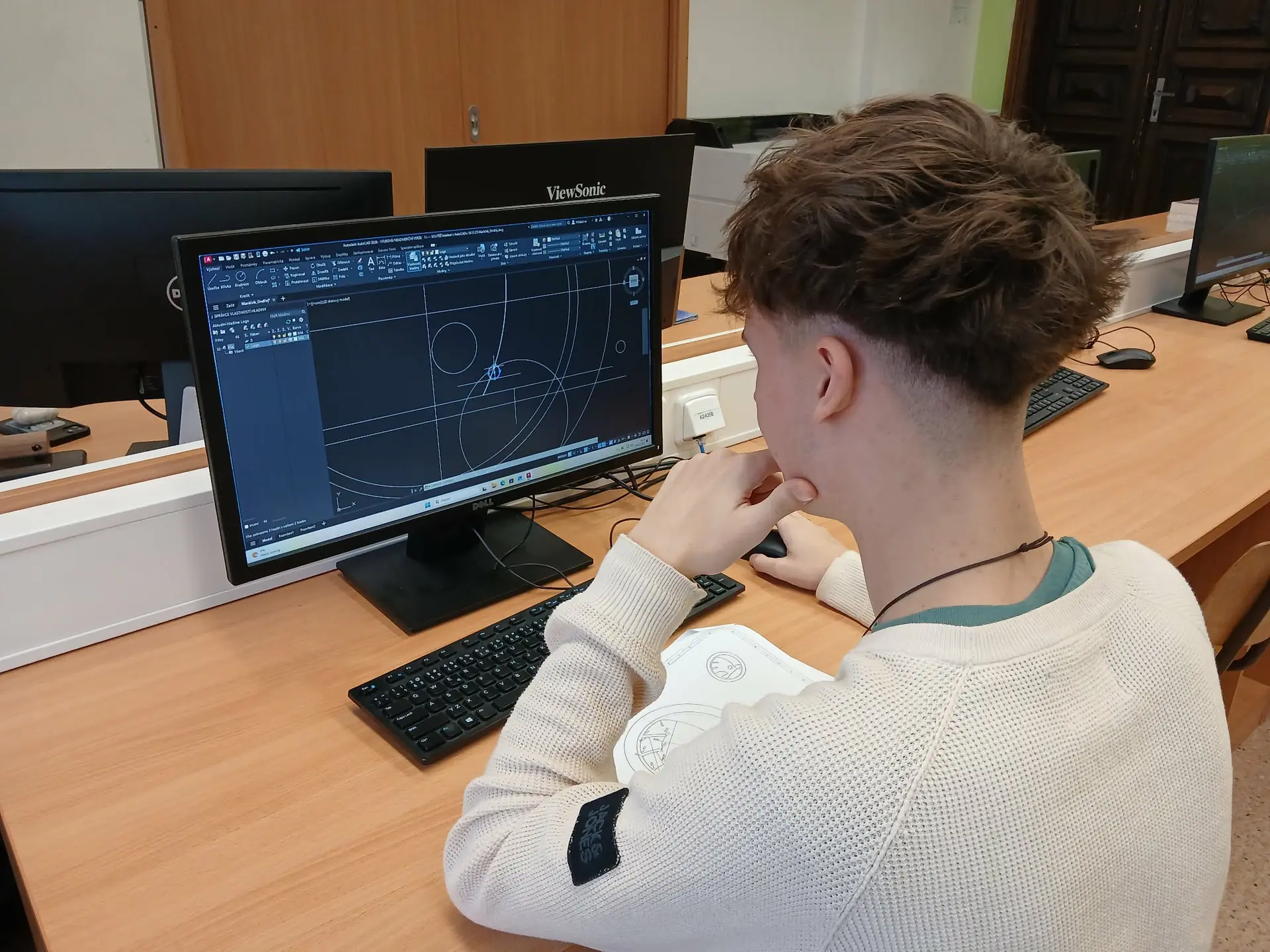 Student sedí u počítače a pracuje na technickém kreslení v CAD softwaru v učebně.