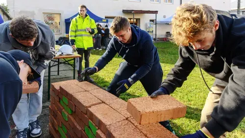 Mladí lidé staví zeď z cihel venku na trávníku během slunečného dne.