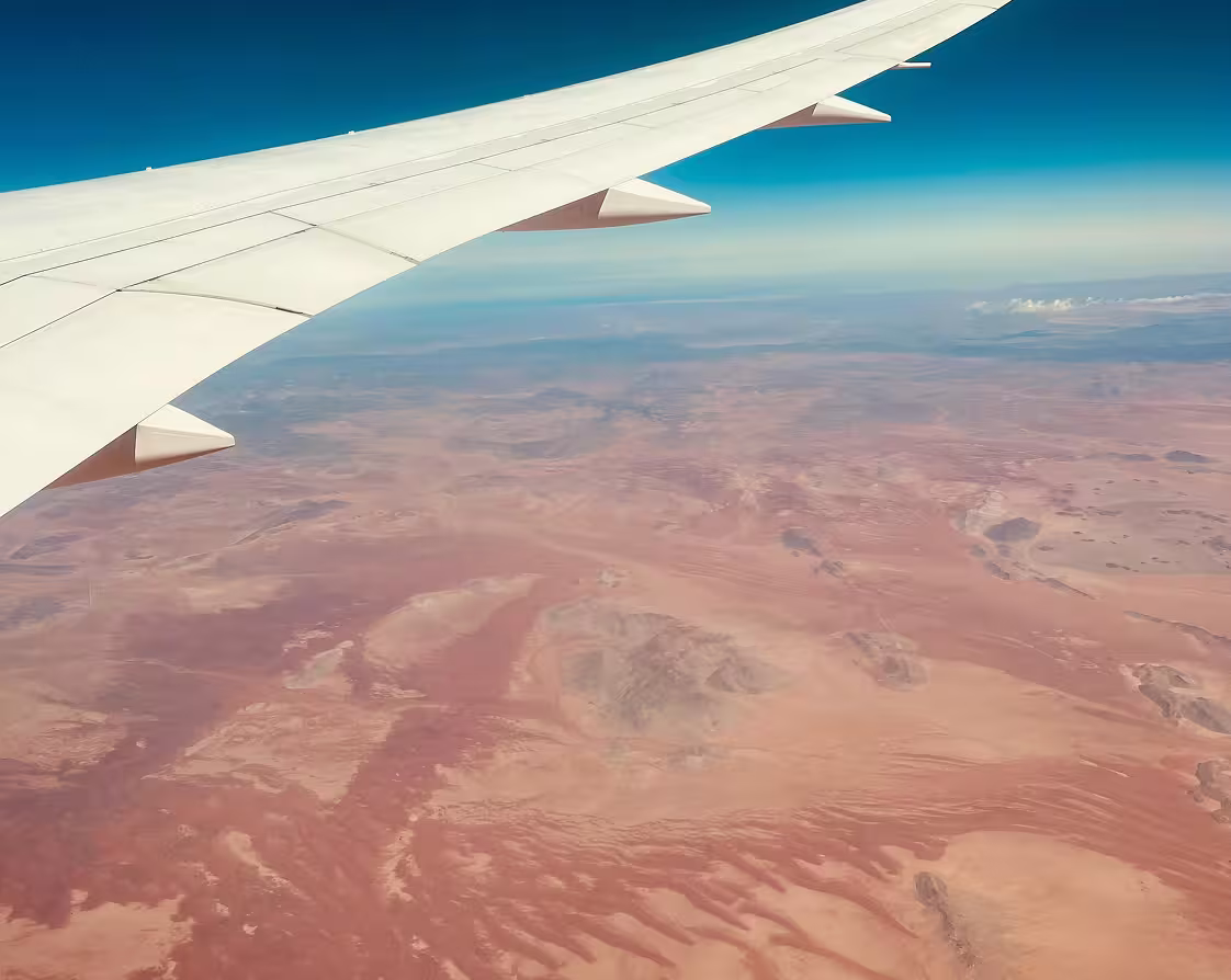 View of desert landscape and clear sky from airplane window showing part of the wing.