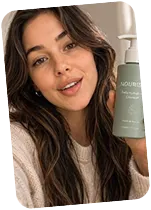Smiling woman with long brown hair holding a green bottle of Nourish skincare product.