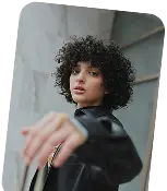 Young woman with curly hair wearing a black leather jacket extending her arm towards the camera.