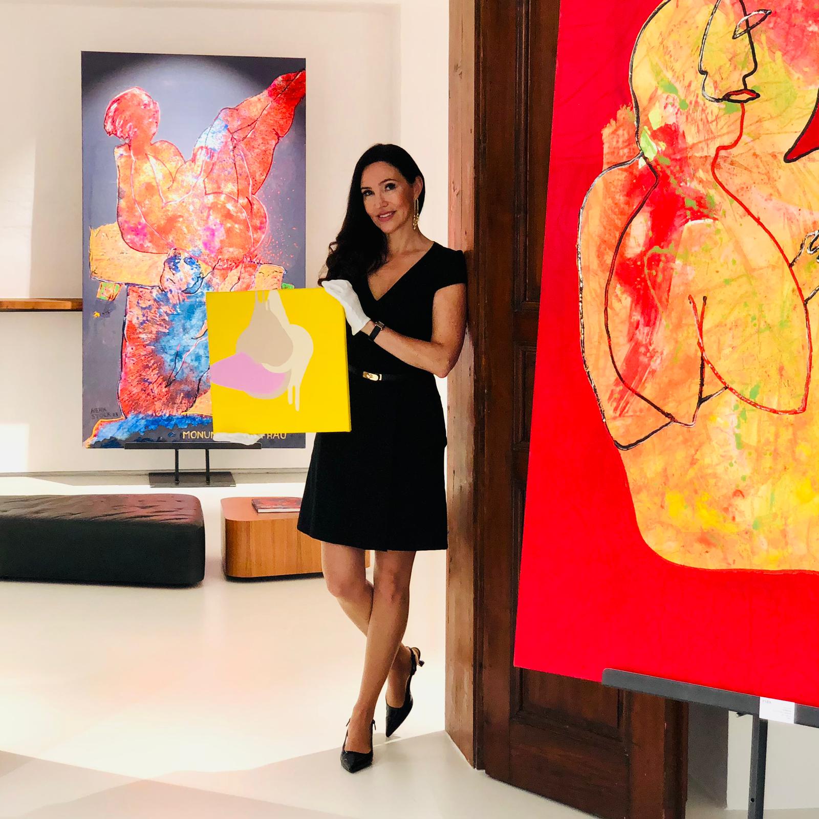Frau in schwarzem Kleid hält kleine abstrakte Kunst vor großen bunten Gemälden in Galerie.