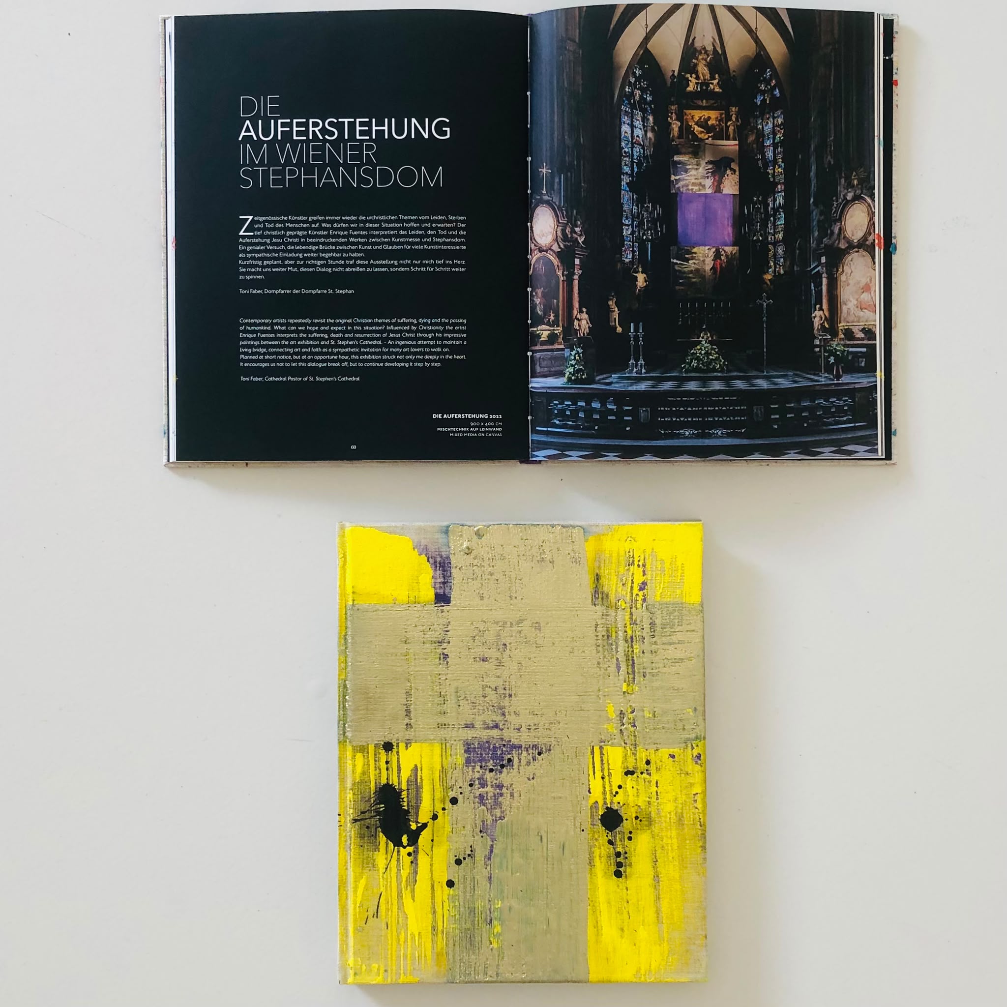 Geöffnete Buchseite über Auferstehung im Stephansdom; darunter ein gelbes abstraktes Gemälde mit Kreuz von Enrique Fuentes in der Park Galerie Buchkirchen von Petuscha Schopper