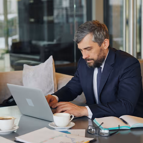 Homme d'affaires concentré travaillant sur un ordinateur portable dans un café moderne avec tisane et documents.