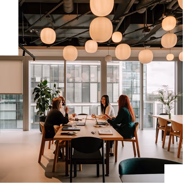 BBC - Quatre femmes en réunion autour d'une table dans un bureau moderne avec suspensions lumineuses.