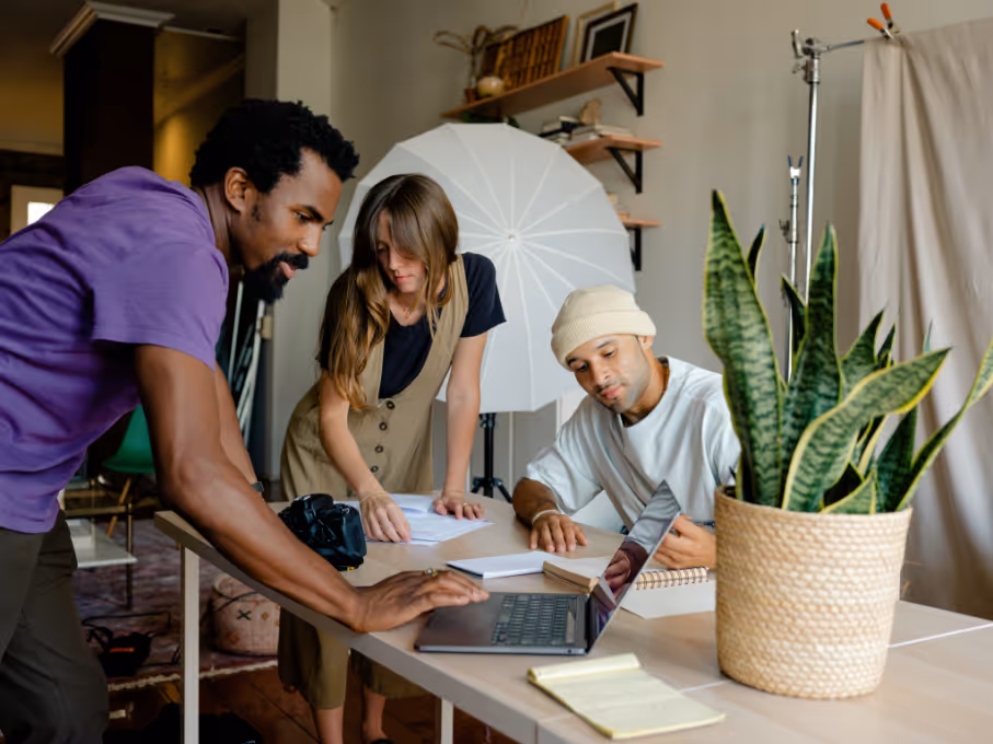 BBC - Trois personnes collaborent autour d'un ordinateur portable dans un bureau avec une plante et du matériel photo.