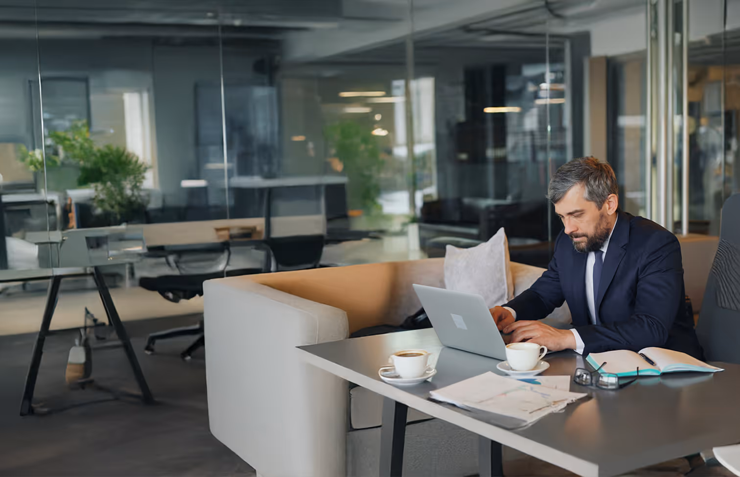 BBC - Homme en costume travaillant sur un ordinateur portable dans un bureau moderne avec café et documents.