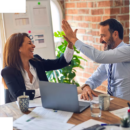 BBC - Un homme et une femme en tenue professionnelle se donnent un high-five souriant à une table de travail.