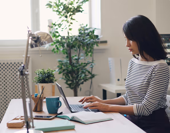 BBC - Jeune femme utilisant un ordinateur portable à un bureau avec plantes et livres.