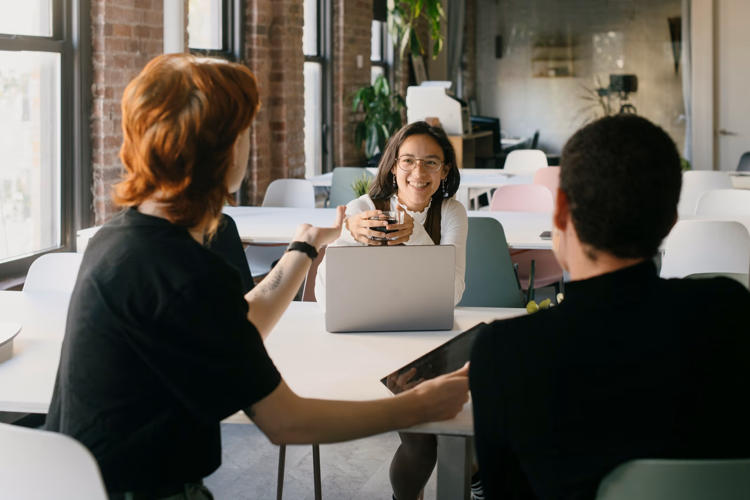 Trois collègues souriants discutent dans un bureau lumineux avec ordinateur portable et tablette.