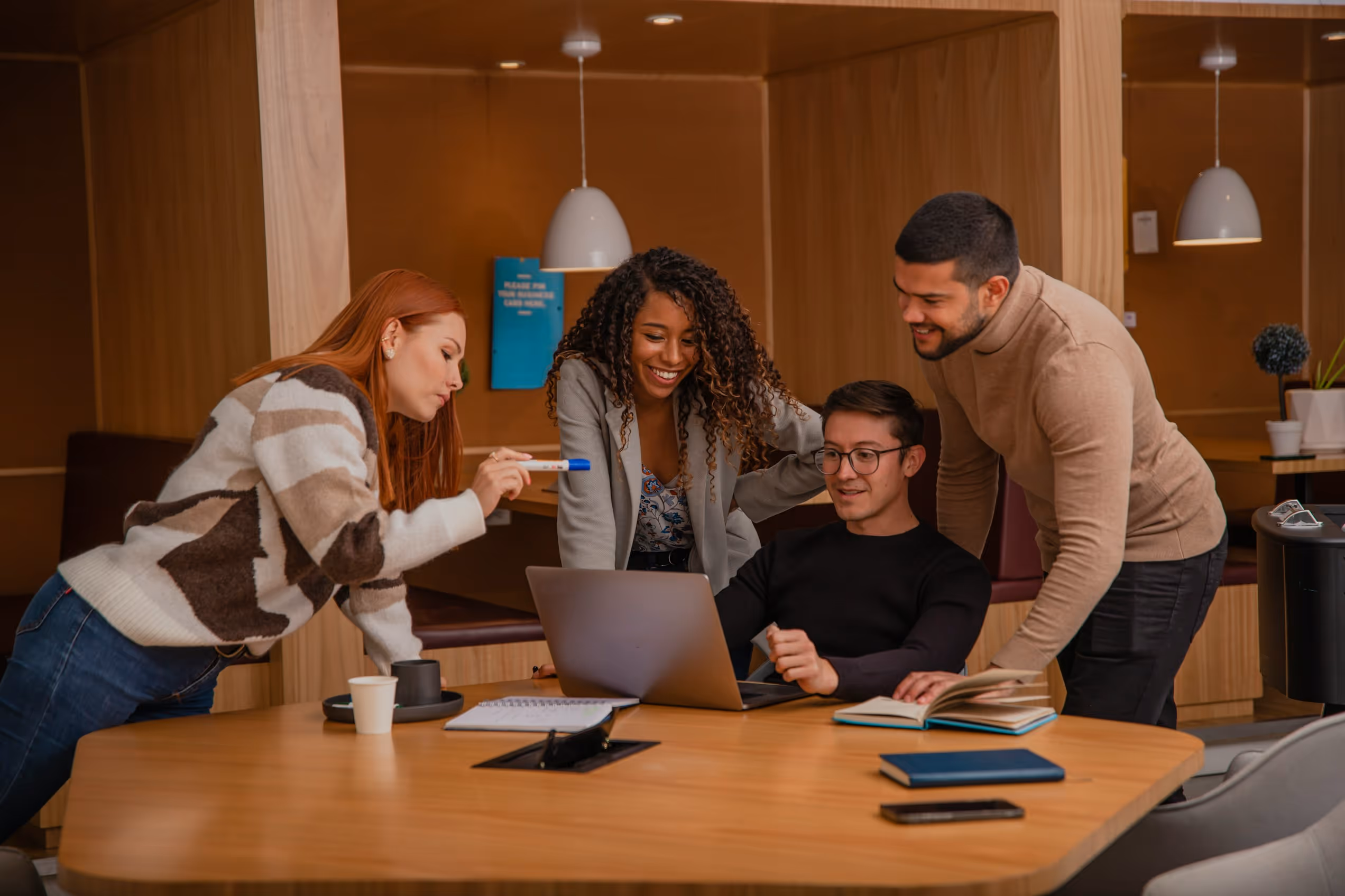Quatre jeunes professionnels regardent un ordinateur portable dans une salle de réunion moderne.