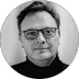 Portrait d'un homme portant des lunettes et un col roulé noir devant un fond clair.