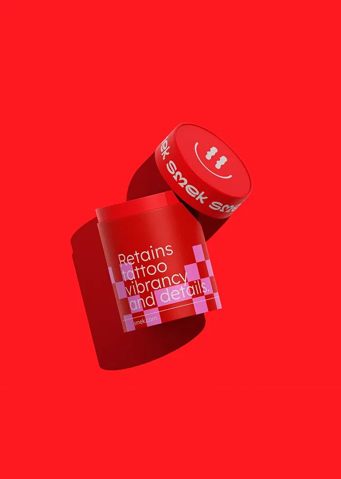 Red jar with a lid featuring a smiley face, text says Retains tattoo vibrancy and details.