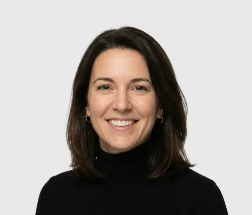 Smiling woman with dark shoulder-length hair wearing a black turtleneck and gold hoop earrings.